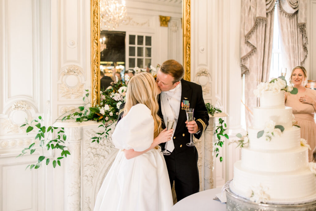 A bride and groom kissing by their cake at their Elms Mansion wedding.