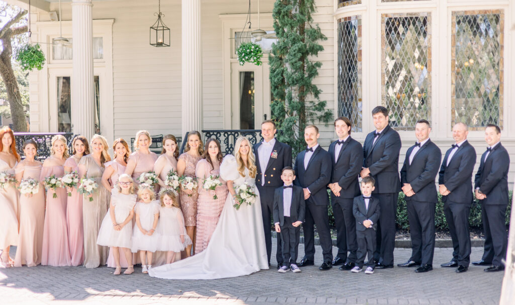A bride and groom stand with their wedding party in front of the Elms Mansion.